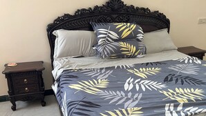 A bed with a dark headboard, a floral-patterned bedspread, and two pillows. There is a small wooden nightstand beside the bed with a single decorative item on it.