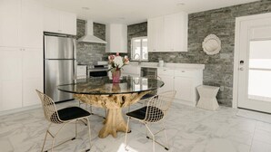 Una cocina moderna con una mesa redonda de vidrio, armarios blancos y un salpicadero de piedra.