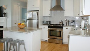 A modern kitchen with white cabinetry, stainless steel appliances, and a central island with stools.