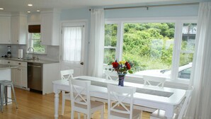 A modern kitchen with white cabinetry, a stainless steel dishwasher, and a dining area with a white table and chairs.