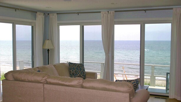 A living room with a beige sofa, a lamp, and a view of the ocean through large windows.