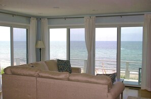 A living room with a beige sofa, a lamp, and a view of the ocean through large windows. - Cozy Oceanfront Cottage with your own beach-no walking needed! (Sandwich)