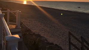 A beach with a wooden walkway leading to the water, a sunset in the background, and a clear sky.