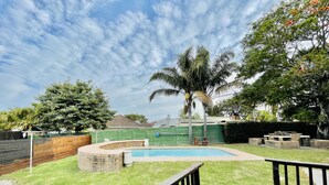 A backyard with a swimming pool, a wooden deck, and a brick patio.