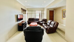 A living room with a flat-screen TV, leather sofas, a coffee table, and a door leading to another room.