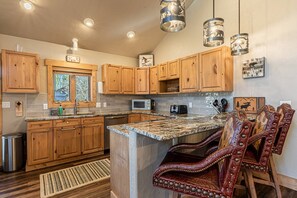 A kitchen with wooden cabinets, a granite countertop, a microwave, and a seating area with leather chairs. - TH w/Private HotTub+Views-Steps to Free Mtn/Town Bus-2 King enSuites-Garage-W/D-Grill-Fireplace (Steamboat Springs)