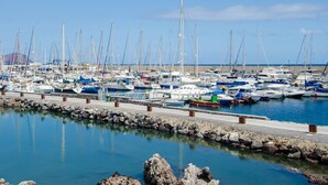Ein Yachthafen mit vielen vertäuten Booten, einer felsigen Küste und ruhigem, spiegelnden Wasser.