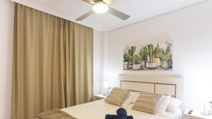 Ein Hotelzimmer mit einem großen Bett, einem Deckenventilator, einem Kaktusgemälde und einem Nachttisch mit Lampe und Fernbedienung.