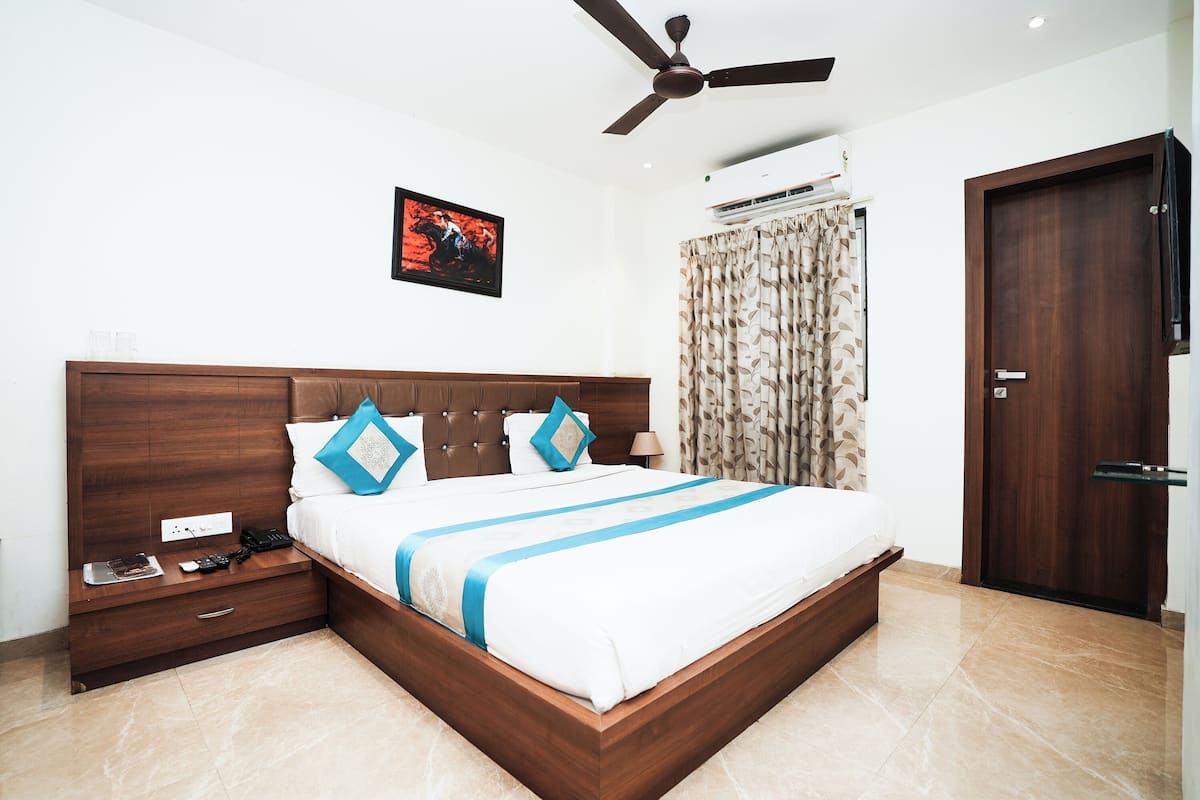 Une chambre d’hôtel moderne avec un grand lit, une tête de lit en bois, un ventilateur de plafond, un appareil de climatisation, une porte et un téléviseur fixé au mur.