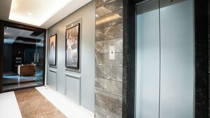 Un couloir moderne avec un sol en marbre, un ascenseur en verre et des tableaux encadrés accrochés au mur.