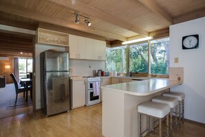 A modern kitchen with a central island, stainless steel appliances, and a large window providing natural light. - Rye Beach House Nestled in Tee Trees (Rye)