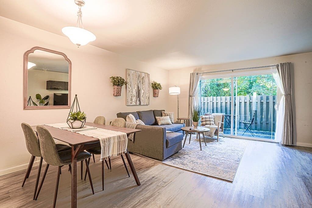 A spacious living area with a dining table, sofas, and a large sliding glass door leading to a balcony.