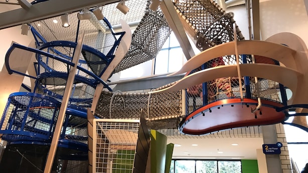En lekplats inomhus med flera nivåer, olika klätterställningar och avdelningar med nät.