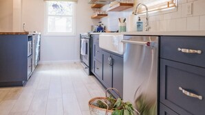 A modern kitchen with dark cabinets, a stainless steel refrigerator, and a window providing natural light. - Charming Renovated Cottage, Perfect Location, Walk to Everything, Across From Park & Cultural Center (Newberg)
