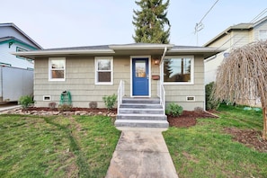 A two-story house with a blue front door, a small front porch, and a number '605' on the door. - Charming Renovated Cottage, Perfect Location, Walk to Everything, Across From Park & Cultural Center (Newberg)