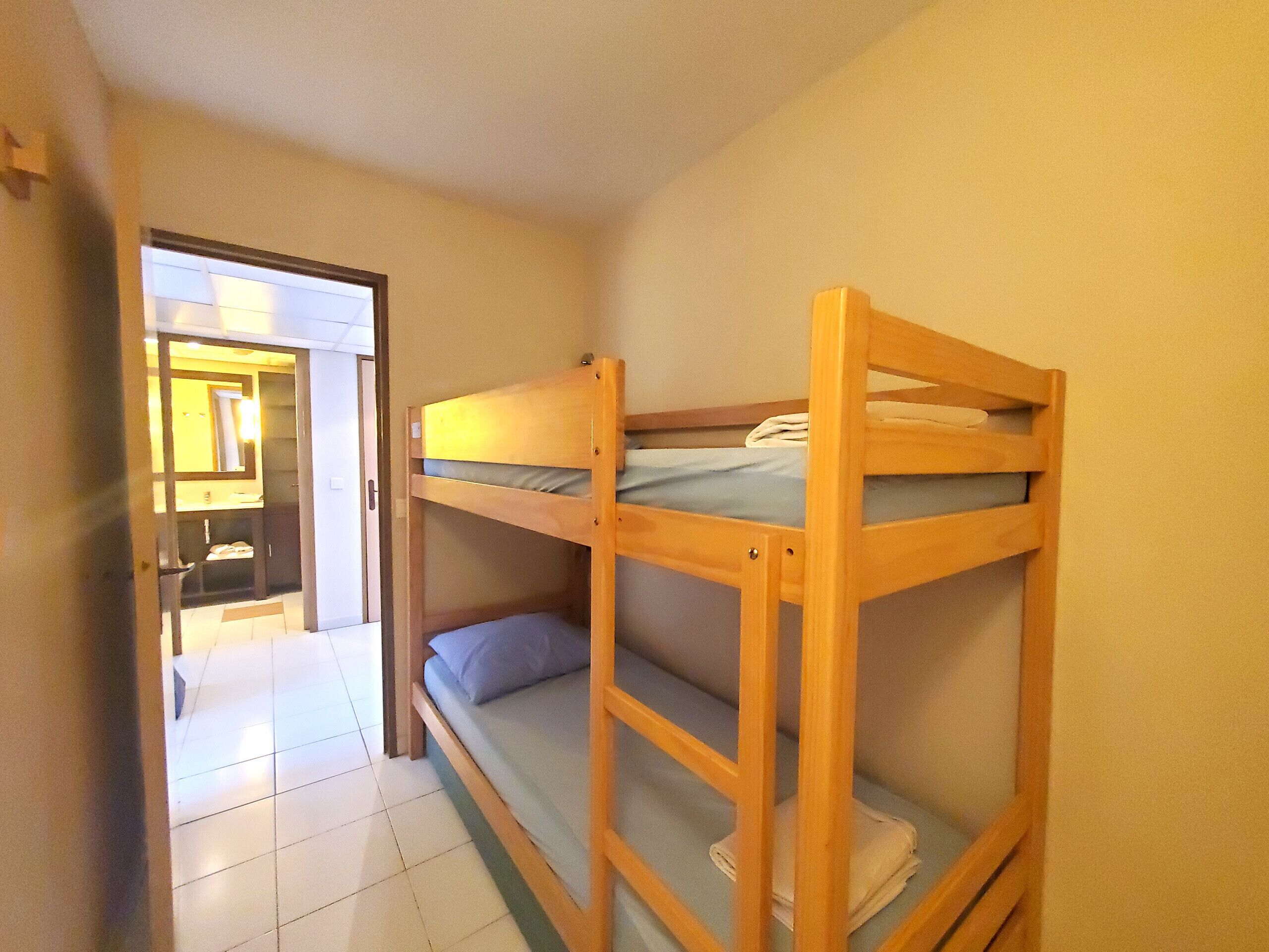 Una habitació amb dos llits superposats, una porta que dona a un bany i un sòl de rajola.