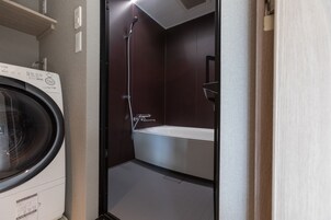 Ein kleines Badezimmer mit Waschmaschine, Badewanne und Dusche.