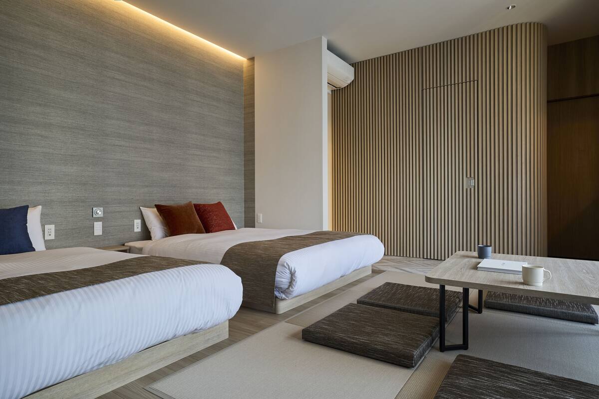 A modern hotel room with two beds, a small table, and a seating area.