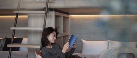 A modern, compact room with a bunk bed, a ladder, and a small table with a book and a candle.