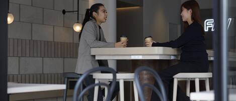 Two people sitting at a table in a modern cafe with a minimalist design, featuring a white table and chairs, and pendant lighting.