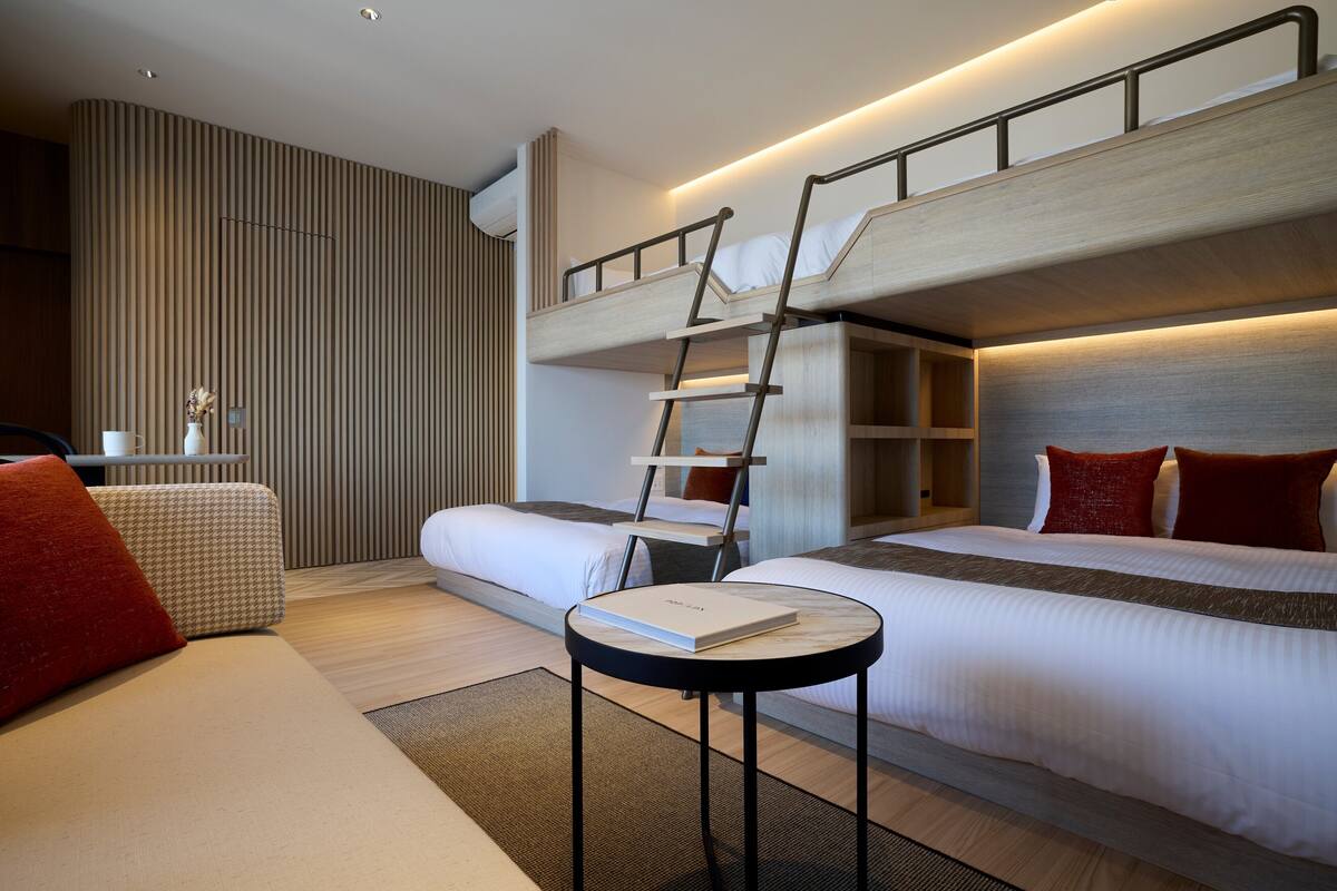 A modern hotel room with a bunk bed, a small table with a book, and a sofa.