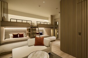 A modern hotel room with a bunk bed, a sofa, a marble coffee table, and a wooden panel wall.