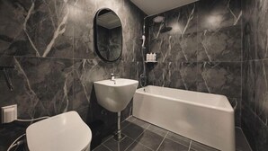 A modern bathroom with a marble wall, a freestanding sink, a bathtub, and a toilet. - Arden Hotel (Cheonan)