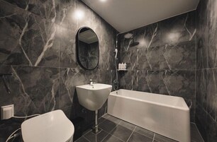Un baño moderno con pared de mármol, lavamanos independiente, bañera y retrete.