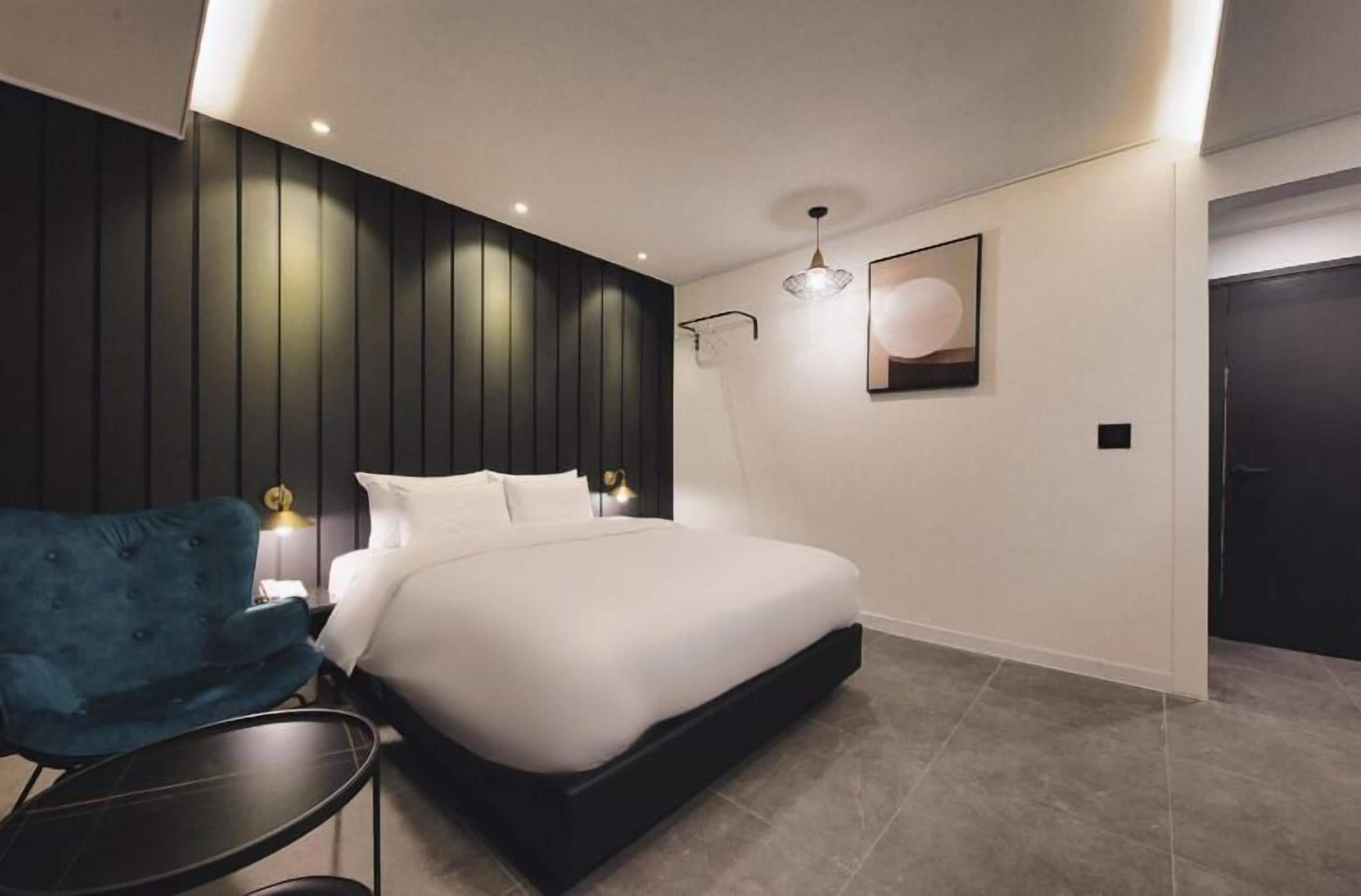 A modern bedroom with a large bed, a blue chair, and a bedside table.