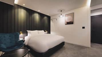A modern bedroom with a large bed, a blue chair, and a bedside table.