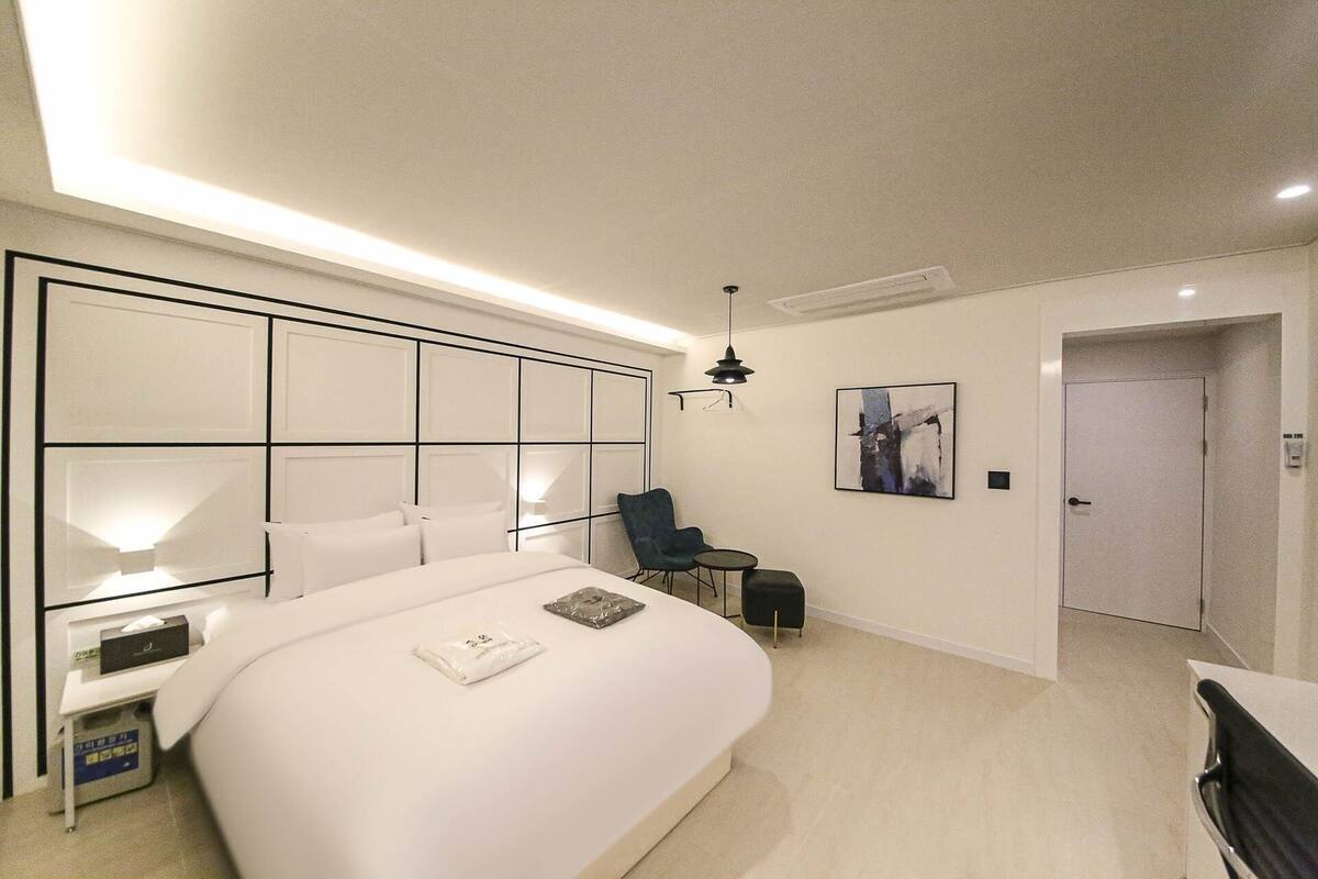 A modern hotel room with a large bed, a desk, a chair, and a small table.