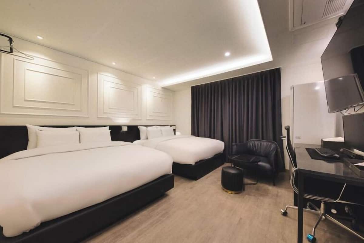 A hotel room with two beds, a desk with a computer, a chair, and a TV.