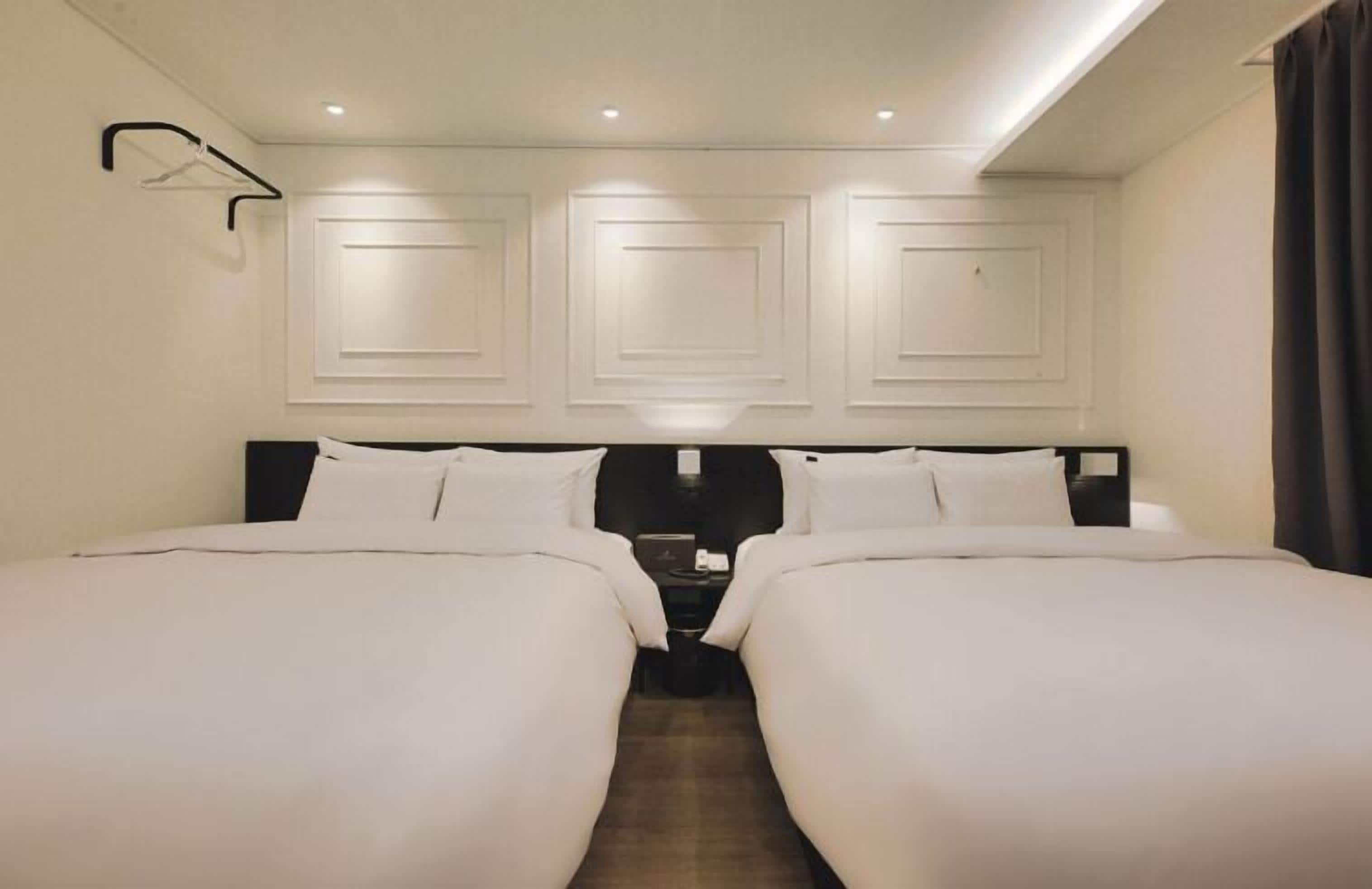 Une chambre d’hôtel avec deux lits, une tête de lit dotée d’un éclairage intégré et un luminaire fixé au mur.