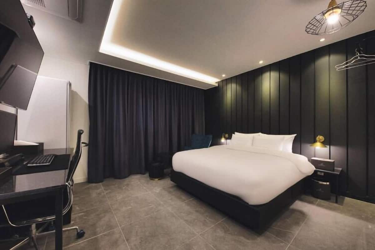 A modern hotel room with a large bed, a desk with a chair, and a wardrobe.