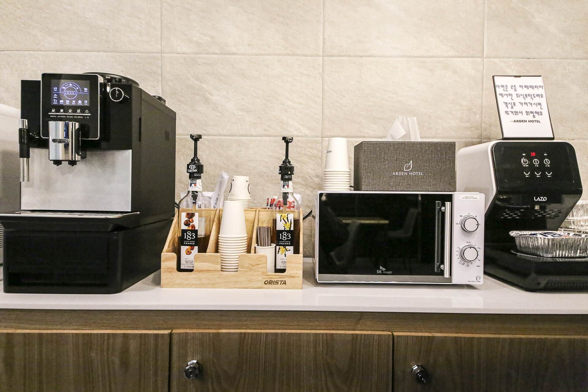 Una encimera de cocina con una cafetera, un microondas y un cartel que indica 'ARDEN HOTEL'.