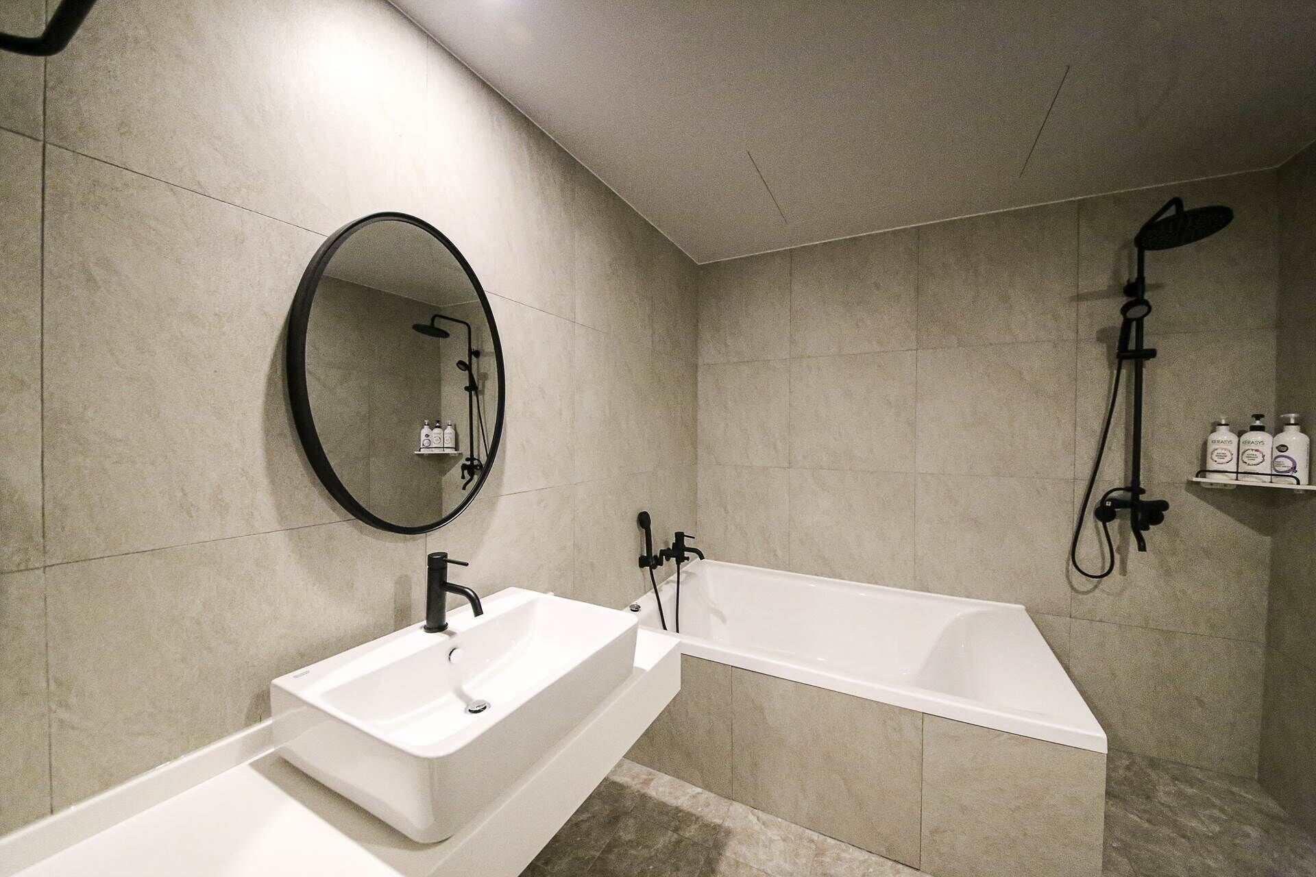 A modern bathroom with a large oval mirror, a white sink, a bathtub, and a shower with a handheld showerhead.