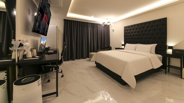 A modern hotel room with a large bed, a desk with a computer, a TV, and a coffee machine. - Arden Hotel (Cheonan)