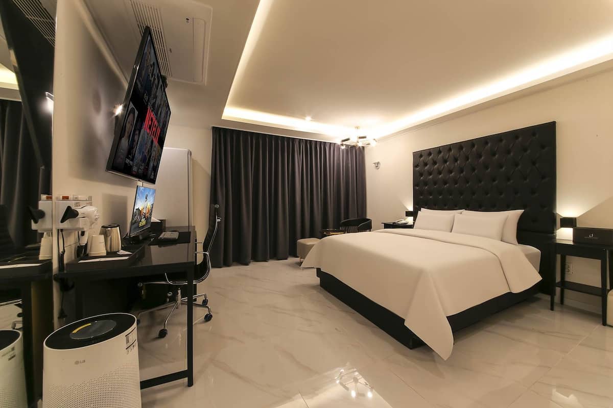 A modern hotel room with a large bed, a desk with a computer, a TV, and a coffee machine.