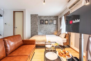 A modern hotel room with a bed, a brown leather sofa, a dining table with plates and glasses, and a flat-screen TV displaying the YouTube logo. - Arita Heights Namba (Osaka)