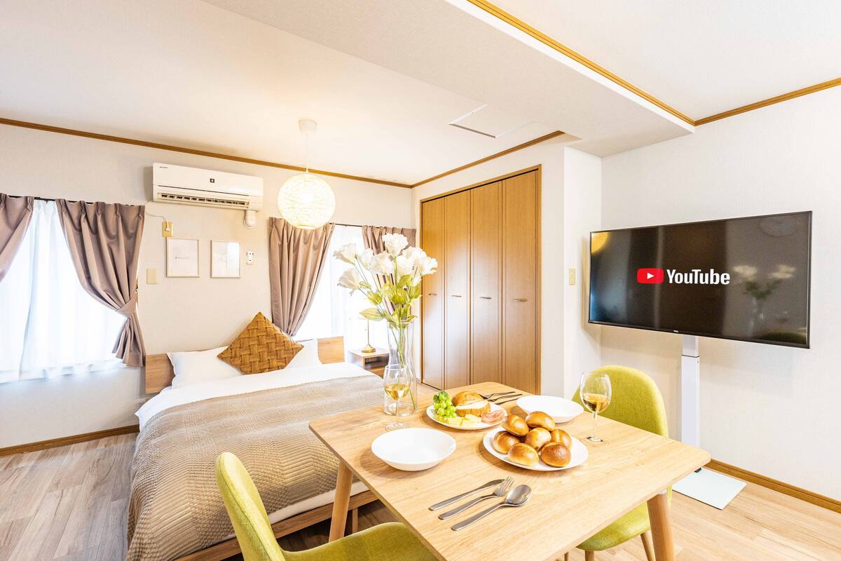 Quarto de hotel com cama, mesa de jantar com pratos e copos, televisão na parede e ar condicionado.