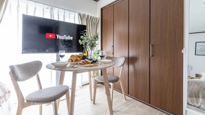 Une chambre moderne dotée d’un coin repas comprenant une table ronde, deux chaises grises et une grande armoire en bois.