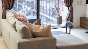 Un salon moderne avec un canapé beige, une table basse en verre et une vue sur un balcon doté d’une balustrade.