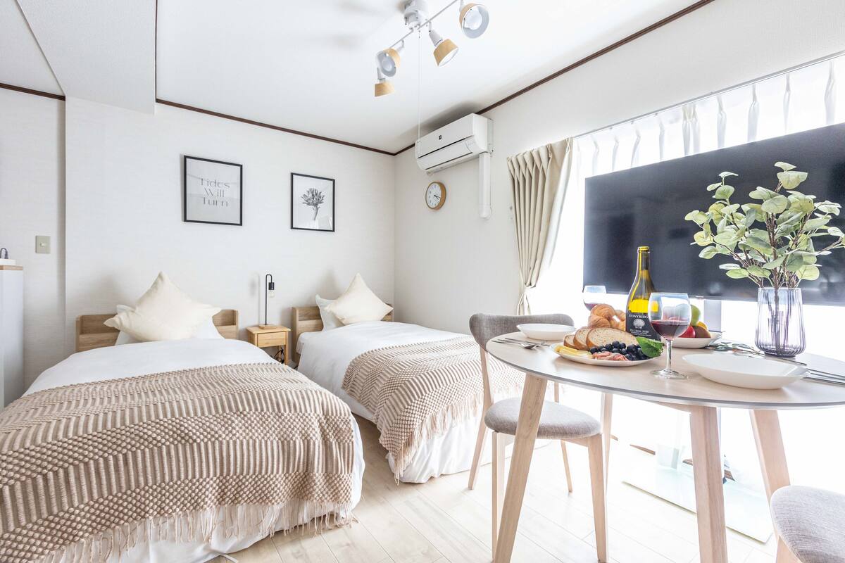 Quarto de hotel com duas camas, uma mesa de jantar com café da manhã, um relógio e um ar condicionado.