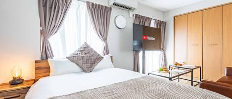 Una habitación de hotel moderna con una cama grande, una mesita de noche con lámpara, una pequeña mesa con artículos de desayuno y un armario.