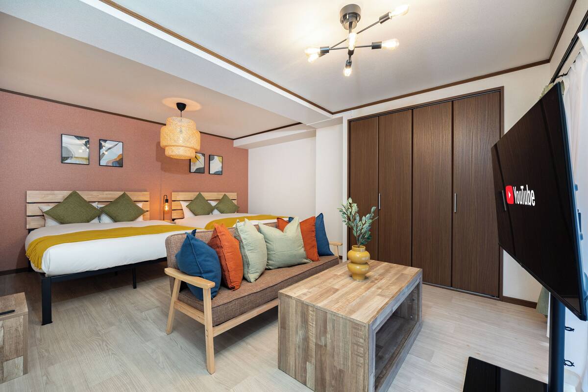 Quarto de hotel moderno com cama, sofá, mesa de centro de madeira e televisão.