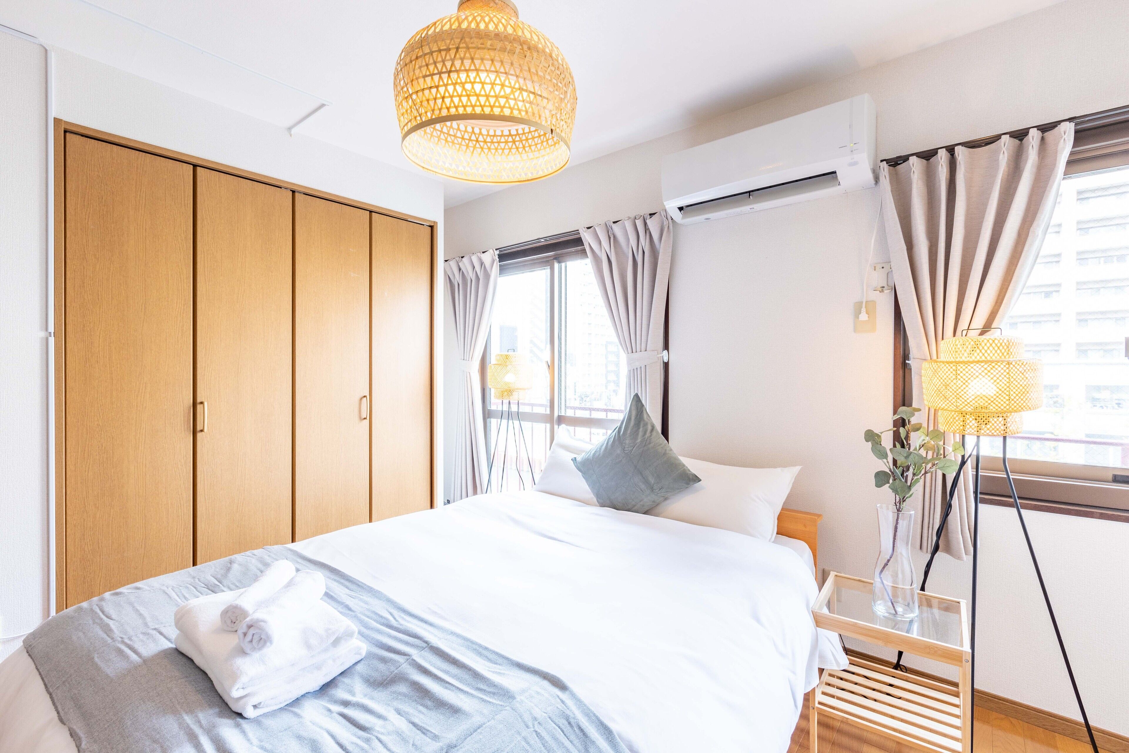 A bedroom with a bed, a wardrobe, a window with curtains, and a hanging light fixture.