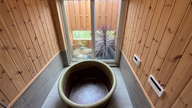 A wooden room with a large stone basin in the center, a sliding glass door leading to an outdoor area with plants, and a thermostat on the wall. - shirahamakashibesso ss2-76 (Shirahama)