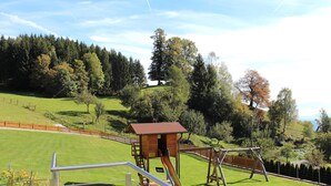 Un parque infantil con tobogán y columpios, rodeado de césped cercado y árboles.