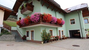 Un bâtiment à deux étages doté d’un balcon orné de fleurs aux couleurs vives, d’un escalier en pierre et d’une cour dallée.