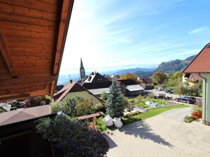 Une vue depuis une fenêtre donnant sur un village avec des maisons traditionnelles, une église et, au loin, une chaîne de montagnes.